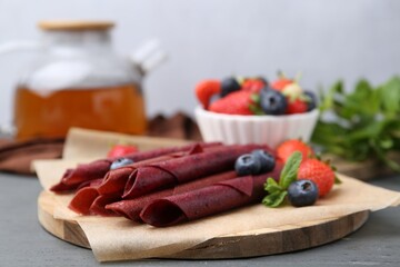 Tasty fruit leather rolls, strawberries, blueberries and mint on grey wooden table, closeup