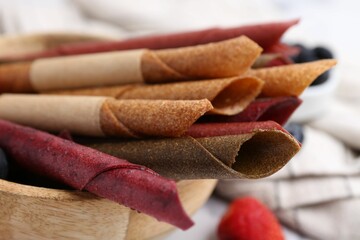 Tasty fruit leather rolls and berries on white table, closeup