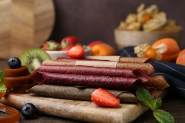 Tasty candied leather rolls, fruits and berries on wooden table, closeup