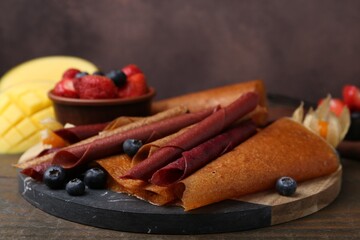 Delicious fruit leather rolls and berries on wooden table, closeup