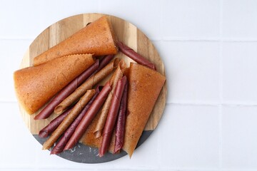 Delicious fruit leather rolls on white tiled table, top view. Space for text