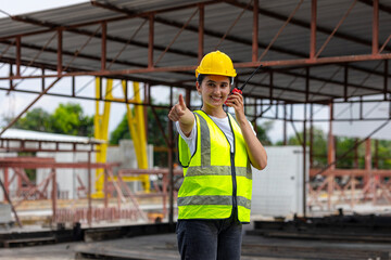 Female civil engineer with walkie talkie shows thumb up and stands next to ready made wall or...