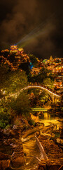 Night view of Wangxian Valley Town with a glowing arched stone bridge over a river, surrounded by traditional Chinese buildings and warm lights in the hillside town.
