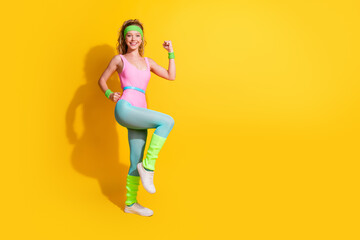 Energetic young woman in colorful retro sportswear striking a pose in front of a bright yellow...