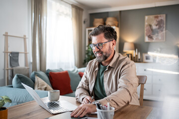 Smiling mature professional working remotely from home office using laptop