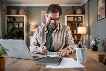 Smiling mature freelancer working from home office taking notes