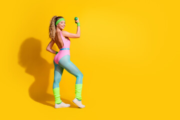 Fototapeta na wymiar Energetic young woman in vibrant retro sportswear posing confidently with a dumbbell against a bright yellow backdrop