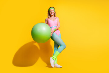 Young woman with exercise ball on vibrant yellow background showcasing active lifestyle and fitness