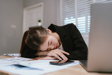 Naklejka premium An overworked Asian businesswoman sits at her office desk, visibly exhausted and stressed, facing deadlines and emotional burnout from workplace pressure.