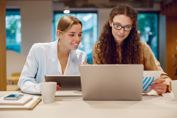 Two professionals are effectively collaborating on a laptop within a welllit and bright office environment