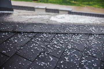 Small hailstones falling and covering a dark shingled roof during a rainstorm.
