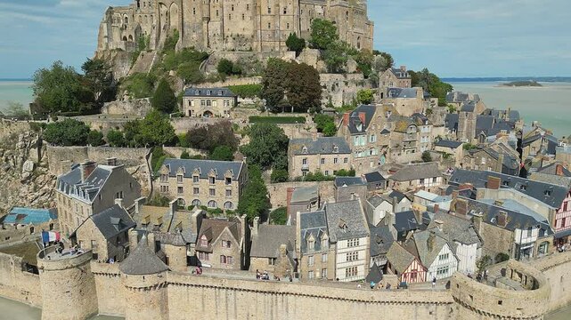Mont-Saint-Michel Abbey with tourists strolling on its walls on a sunny day with cloudy sky, France