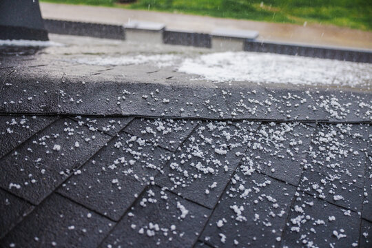 Small hailstones falling and covering a dark shingled roof during a rainstorm.