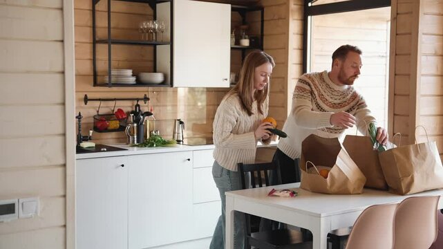 Mother and father take out groceries from bags, he hands bananas to his son who is walking next to him, in the kitchen