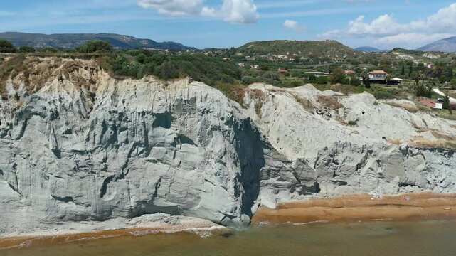 Aerial drone footage of Xi Beach in Kefalonia, Greece, showcasing its iconic clay coastline, bright orange sands, and arid Mediterranean landscape. Captured on a sunny day along the Ionian Sea.

