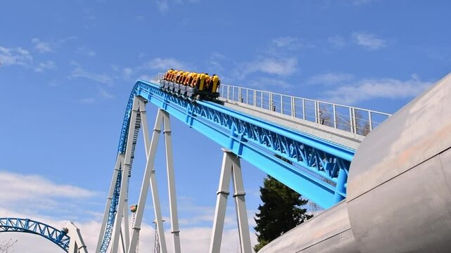 Roller coaster climbing blue track under clear sky with riders in yellow seats ready for thrilling drop in amusement park.