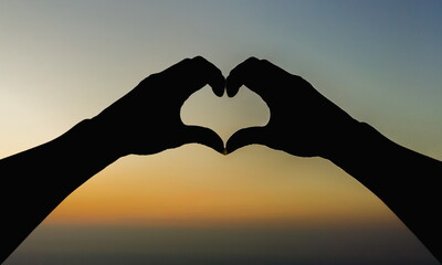 A silhouette of a young woman raising her hands above her head to represent a heart symbol...