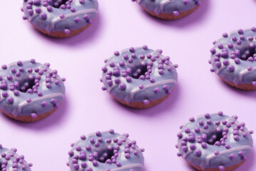 Pattern of purple glazed donuts on a purple background. Sweet treat or dessert concept