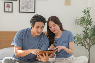 Young Asian couple shopping online while using digital tablet at home, Couple using credit card to pay bills or to book a room for vacation, making an online purchase