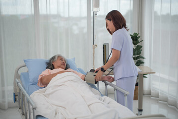 Asian nurse with tonometer measuring woman patient's blood pressure at hospital