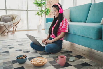 Young woman in casual style enjoying leisure time indoors while working on a laptop, sitting on a...