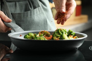 Woman adding spices to dish in kitchen, closeup