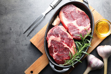 Pieces of raw beef meat with spices in baking dish, oil and fork on gray textured table, flat lay