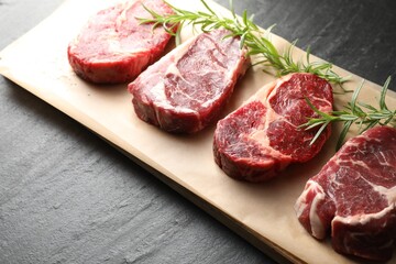 Pieces of raw beef meat and rosemary on black table, closeup