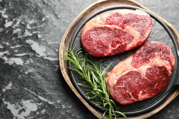 Pieces of raw beef meat and rosemary on dark table, top view. Space for text