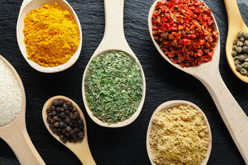 Different aromatic spices in spoons on black table, closeup