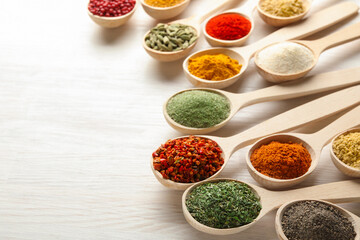 Different aromatic spices in spoons on white wooden table, closeup. Space for text