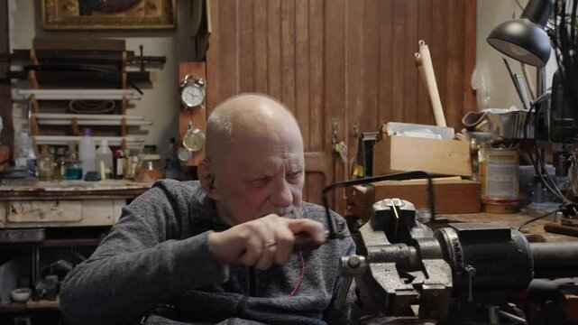 Senior elderly master jeweler in wheelchair works in a workshop