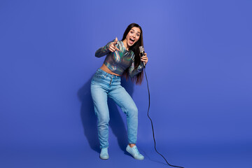 Young vibrant woman with microphone on purple background, expressing joy and energy in casual trendy fashion