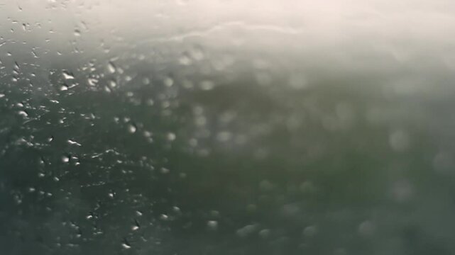 Foggy car window covered with rain drops, moisture and condensation obscure outside view, creating cold and moody atmosphere.