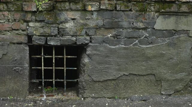 An old stone and brick wall with a small window barred by metal bars. Architectural detail of an old building, close-up view. High quality 4k footage