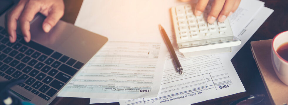 Budget and Tax planning concept. Accountant hand using calculator and laptop, and reviewing tax forms. Represents personal finance, tax preparation, budgeting, and season to pay tax-banner image.