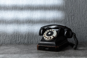 Vintage black telephone with rotary dial on gray stone table.