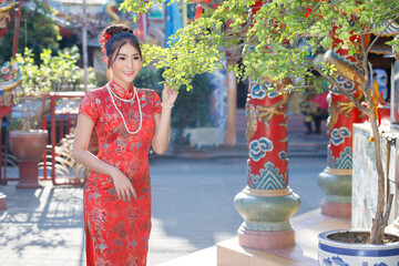 Beautiful Asian woman in traditional red cheongsam smiling in a Chinese temple courtyard. Concept of culture, celebration, Chinese New Year, and traditional fashion.