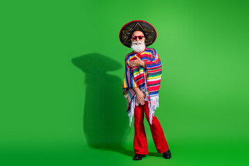 Elderly man in festive Mexican poncho and sombrero on green backdrop gesturing energetically, celebrating tradition and culture
