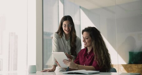 Two happy female colleagues discussing online product on tablet, using digital gadget for teamwork, professional discussion. Internet project manager asking expert for consultation