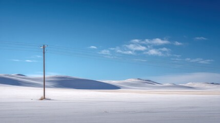 Winter Solitude: A lone utility pole stands sentinel in a vast, snow-covered landscape under a brilliant blue sky.