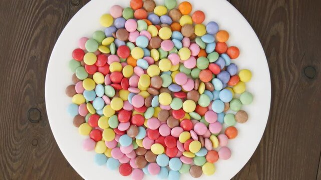 Colorful smarties spinning on white plate, showcasing vibrant candy rotation with pastel rainbow hues against clean studio background.