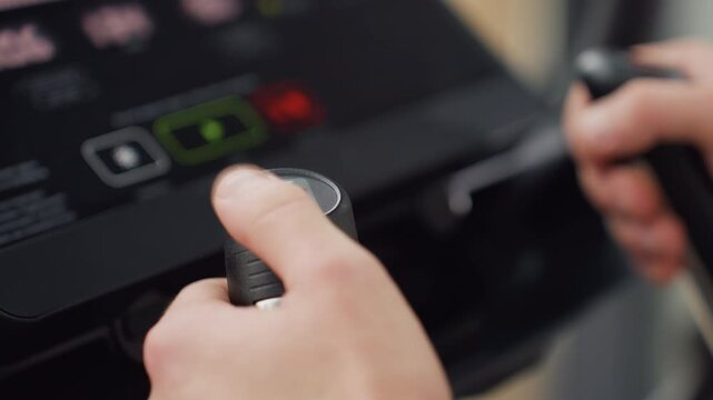 Firm grip with both hands of man on movable handle pressing control knob to adjust speed on elliptical console in bright modern gym under natural light showcasing focused intensity adjustment