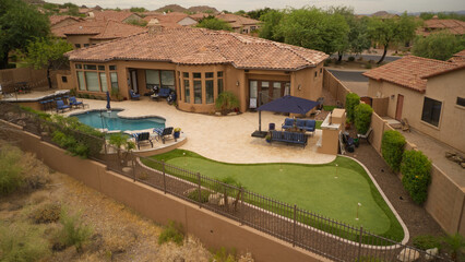 an aerial view of a desert landscaped backyard featuring a travertine tiled pool deck, putting green, outdoor kitchen and fireplace.