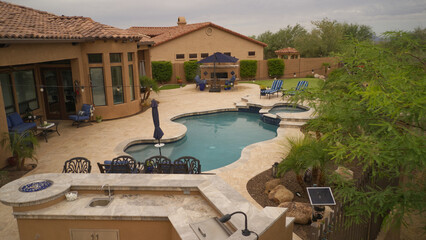 an aerial view of a desert landscaped backyard featuring a travertine tiled pool deck, putting green, outdoor kitchen and fireplace.