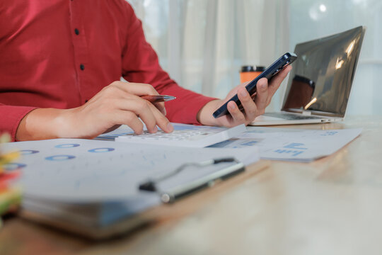 A focused businessperson works on summarizing annual performance results while multitasking by replying to client messages on a smartphone.