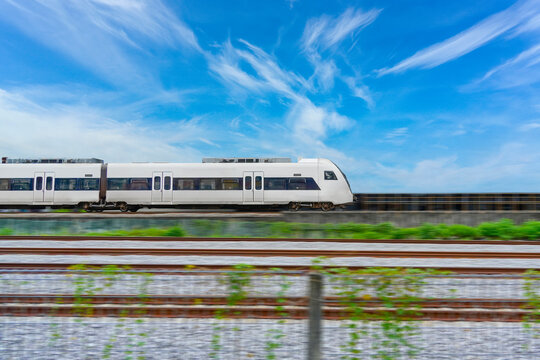 Speed modern commuter train, motion blur rides among the fields and green vegetation. with blue sky clouds, side view.