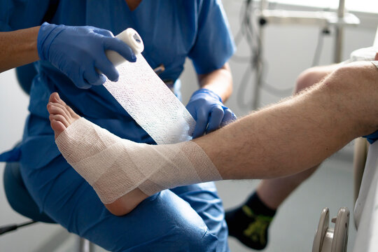 Nurse bandaging patient's injured ankle in hospital room