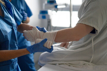 Nurse bandaging patient's hand in hospital room