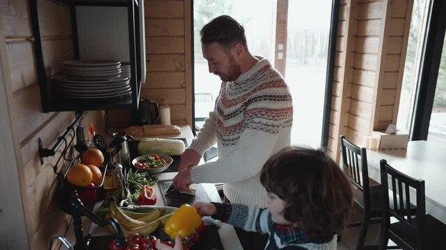 A father chops cabbage while his son washes bell peppers next to him